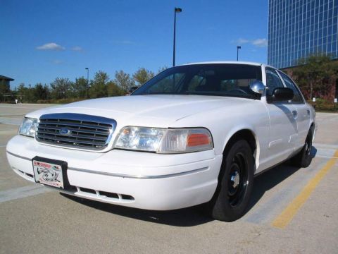 1998 Ford Crown Victoria - A white sedan is parked in a lot with a modern building in the background.