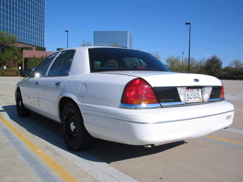 White sedan parked outside a building. Rear view shows license plate and 'Crown Victoria' text