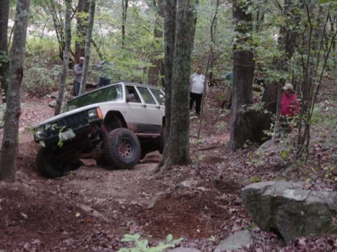 1991 Ford Bronco - A modified Jeep Cherokee XJ navigates a challenging off-road course through a wooded area.
