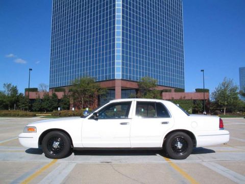 1998 Ford Crown Victoria - White 1998 Ford Crown Victoria parked on pavement with a tall glass building in the background.