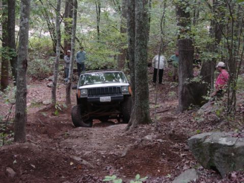 1991 Ford Bronco - A white Jeep Cherokee XJ navigates a wooded trail with several people observing.