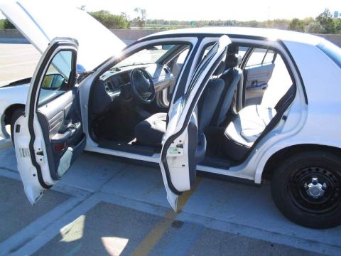 1998 Ford Crown Victoria - The interior of a white sedan is visible with all doors and the hood open, revealing the seats and dashboard.