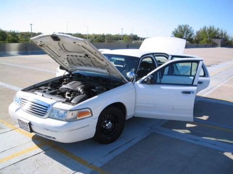 1998 Ford Crown Victoria - A white 1998 Ford Crown Victoria is parked with its hood and driver's door open, revealing the engine compartment.