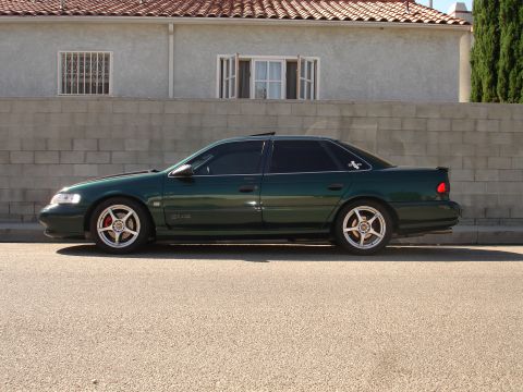 1993 Ford Taurus - Side profile of a dark green 1993 Ford Taurus with aftermarket wheels.