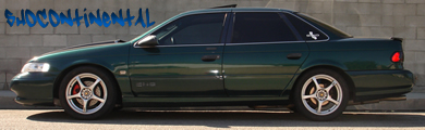 1993 Ford Taurus - Side profile of a 1993 Ford Taurus sedan with custom wheels against a brick wall.