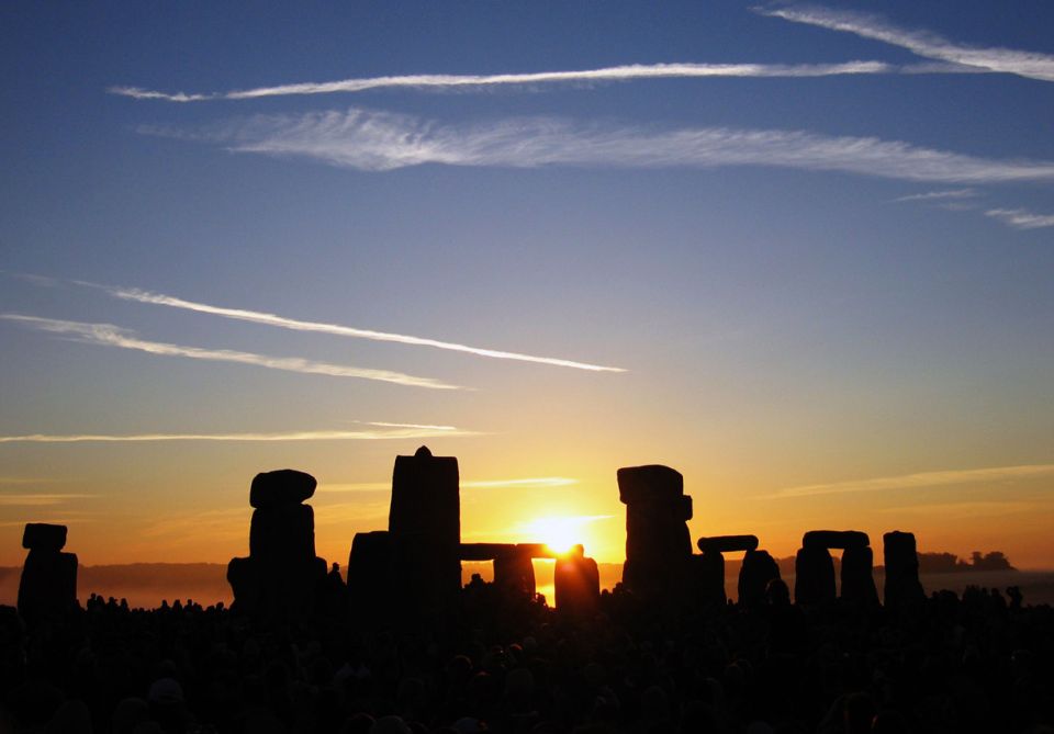 Stonehenge silhouette against sunrise sky with contrails