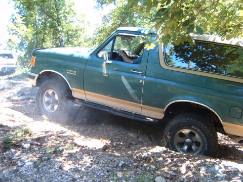 1988 Ford Bronco - This green Ford Bronco is navigating a rough, off-road terrain with a second vehicle in the distance.