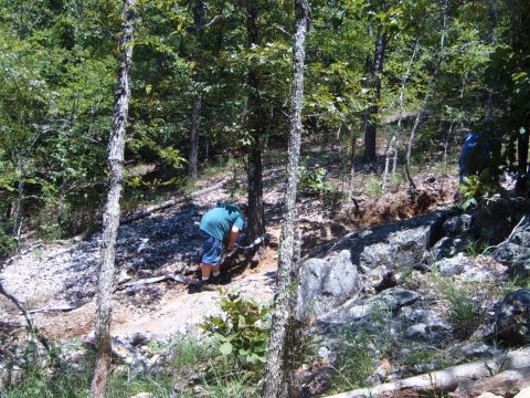 1988 Ford Bronco - A person is digging in a wooded area with rocks and trees visible.