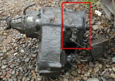 1991 Ford Bronco - Transfer case covered in mud, resting on a bed of gravel.