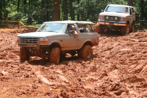 1990 Ford Bronco - Two Ford Broncos navigate a muddy off-road course.
