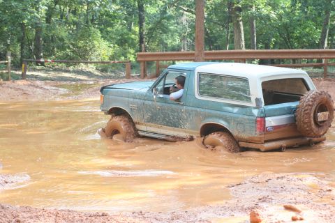 1990 Ford Bronco - Ford Bronco navigating a muddy trail, tires deep in the mire.