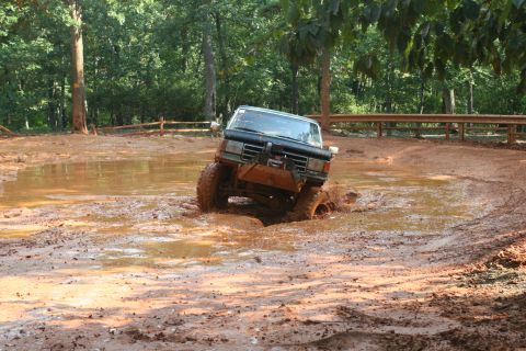 1990 Ford Bronco - This vehicle is navigating a challenging muddy terrain, with its tires deep in the mire.