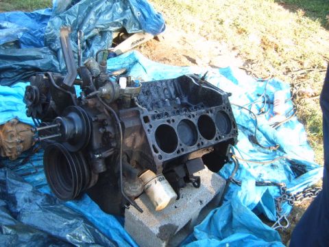 1988 Ford Bronco - Engine block with cylinders exposed, resting on concrete blocks and blue tarp, with a filter visible.