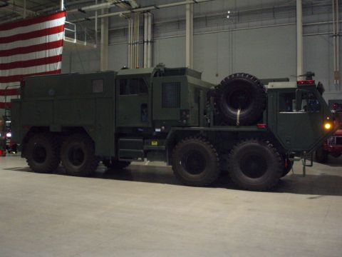 1981 Ford Bronco - A large, multi-axle military truck is parked indoors with an American flag in the background.