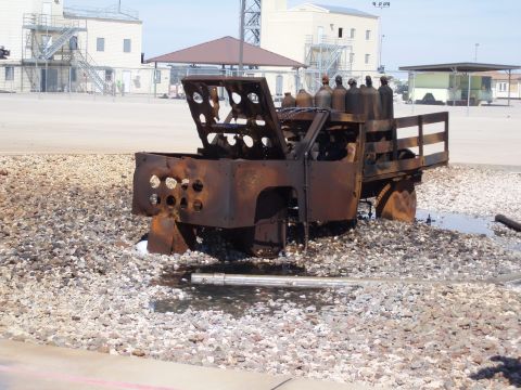 1981 Ford Bronco - A severely damaged truck, likely used for transporting gas cylinders, sits abandoned on a gravel lot.