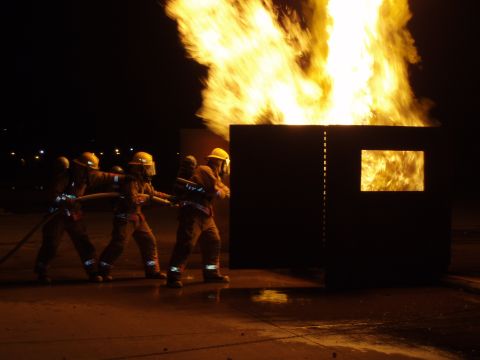 1981 Ford Bronco - Firefighters train with a hose during a nighttime exercise in front of a burning structure.