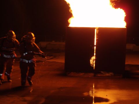1981 Ford Bronco - Firefighters train with hoses near a large, contained flame during a fire school exercise.