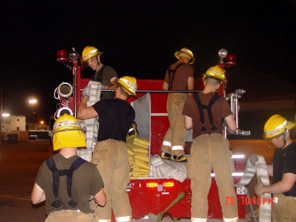 Firefighters handling hoses on the back of a red truck at night