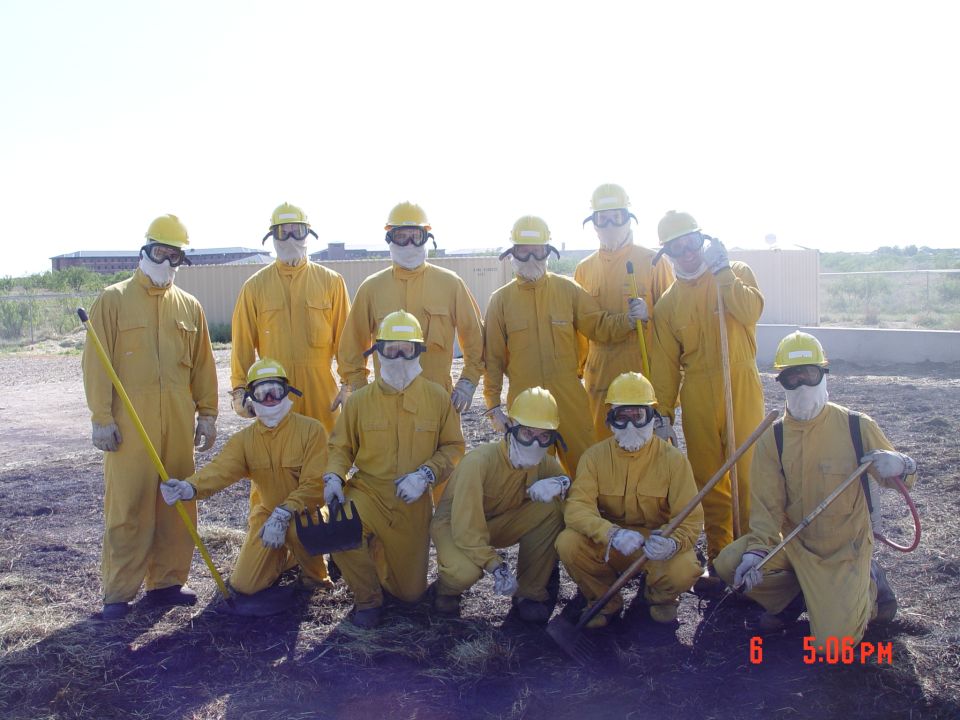 Group of ten people in yellow protective suits and helmets, some holding tools, posing outdoors