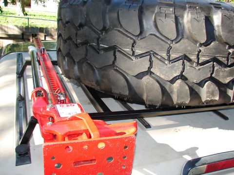1996 Ford Bronco - A Hi-Lift jack is secured next to a spare tire on a vehicle's roof rack.
