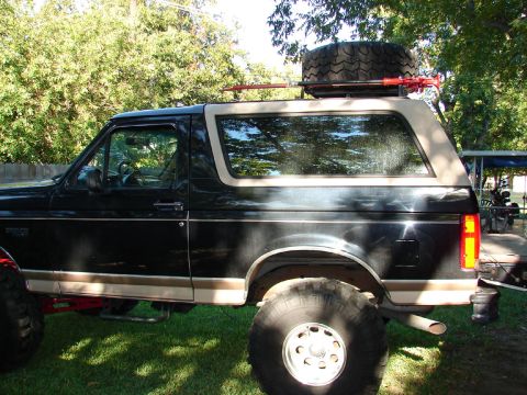 1996 Ford Bronco - Side view of a lifted black Ford Bronco with a spare tire mounted on a roof rack.