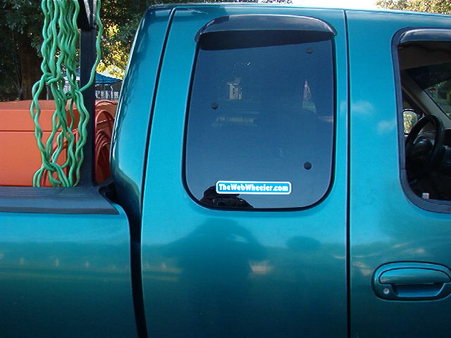 Teal extended-cab pickup side view with TheWebWheeler.com sticker on tinted rear cab window