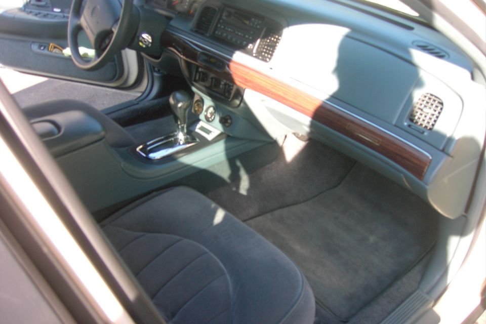 Sedan interior with cloth seats, console shifter, and wood-grain dash trim, seen through open door.