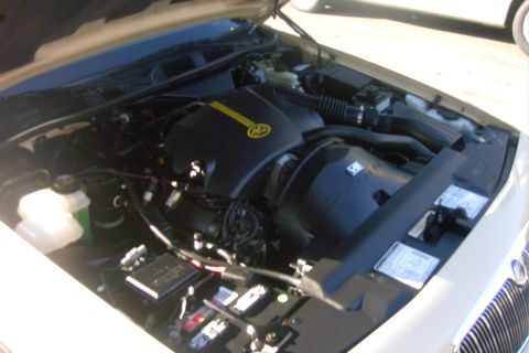 1996 Mercury Grand Marquis - Engine bay of a white vehicle with the hood raised, showing a black plastic engine cover marked with a yellow K&N stripe and a 'V8' badge,…
