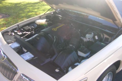 1996 Mercury Grand Marquis - Under-hood view of a white sedan's V8 engine bay with black plastic intake and air cleaner assembly, brake master cylinder and reservoir on…