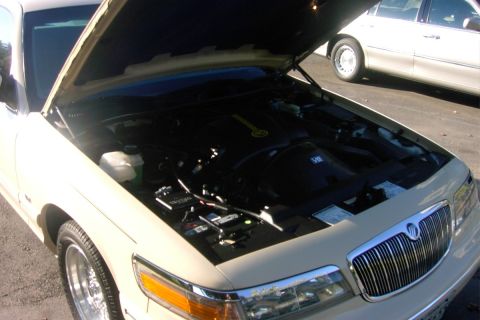 1996 Mercury Grand Marquis - Front three-quarter view of a white/cream Mercury sedan with the hood open, revealing a V8 engine bay with a yellow-labeled component and v…