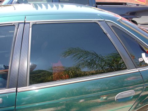 1993 Ford Taurus - Side view of a green 1993 Ford Taurus, showing a reflection of palm trees in the tinted window.