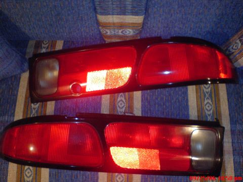 1997 Ford Probe - A matched left and right pair of removed red tail lamp assemblies laid face-up on a blue and tan striped upholstered couch, each with a cle…
