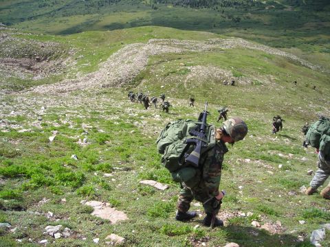 2003 Jeep TJ - A group of soldiers ascend a rocky, green mountain slope, carrying heavy gear.