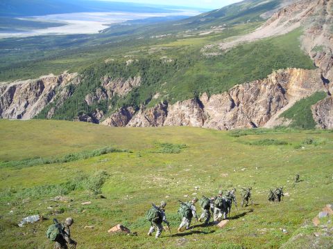 2003 Jeep TJ - Soldiers navigate a challenging terrain, ascending a steep, grassy mountainside with a vast valley in the background.