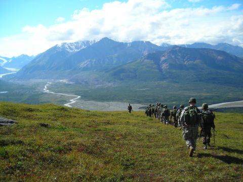 2003 Jeep TJ - A group of soldiers marches across a vast, mountainous landscape under a partly cloudy sky.