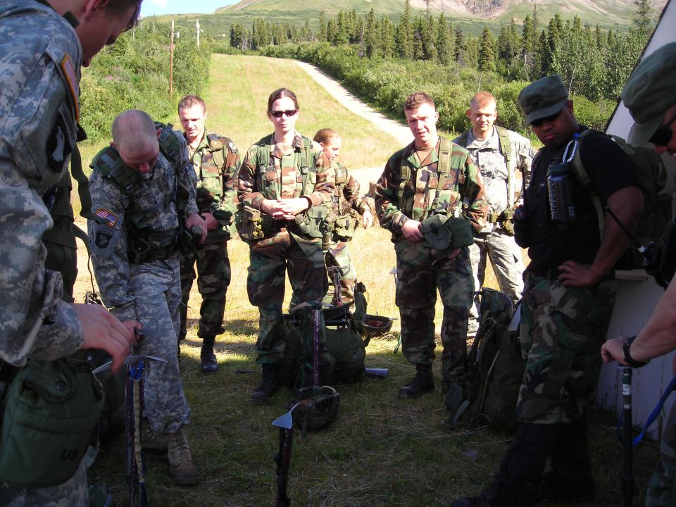 Military personnel gathered outdoors with backpacks and equipment
