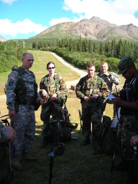 2003 Jeep TJ - Soldiers gather outdoors with a scenic mountain backdrop under a bright blue sky.