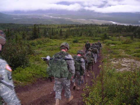 2003 Jeep TJ - A line of soldiers marches along a trail in a vast, green wilderness under a cloudy sky.