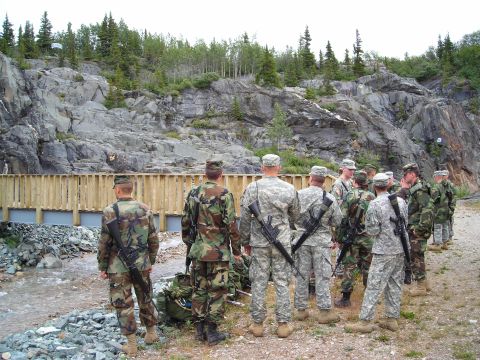 2003 Jeep TJ - Soldiers gather near a bridge in a rocky, wooded area.