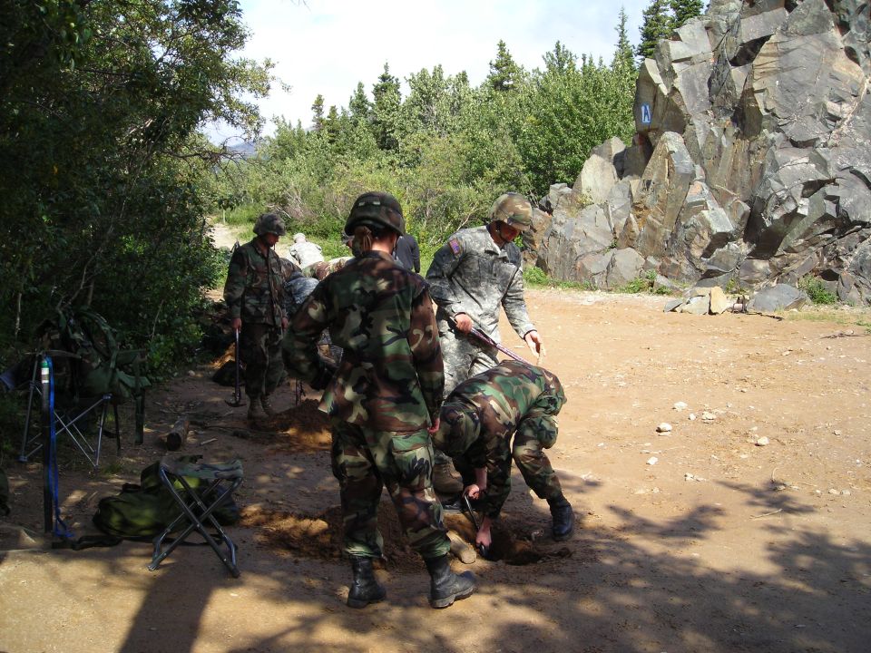 soldiers in camouflage uniforms digging in the dirt near a rocky hillside and trees