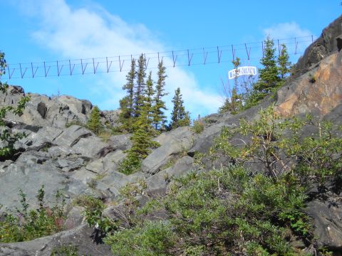 2003 Jeep TJ - A pedestrian suspension bridge spans a rocky cliff face under a blue sky with scattered clouds.