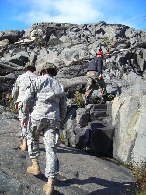2003 Jeep TJ - Three individuals in military attire ascend a , rocky terrain on a clear day.