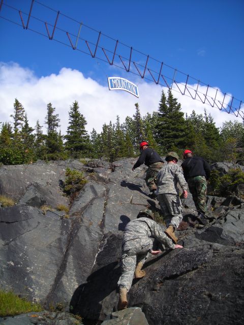 2003 Jeep TJ - Soldiers ascend a rocky incline beneath a suspended structure, with a sign indicating "MOUNTAIN" overhead.
