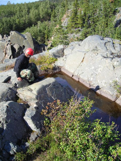 2003 Jeep TJ - A person in a red helmet observes a natural rock pool surrounded by dense foliage and rocks.