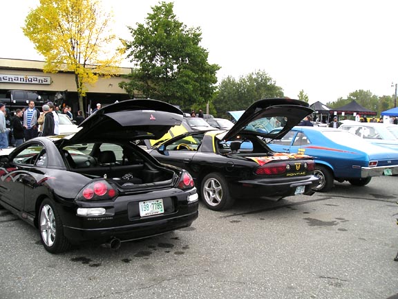 Black Pontiac Trans Am with trunk open, next to a black Mitsubishi Eclipse with trunk open, and a blue sedan