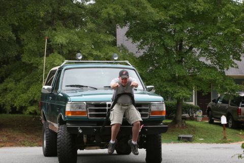 1996 Ford Bronco - A man sits on the hood of a lifted green Ford Bronco, with another SUV visible in the background.