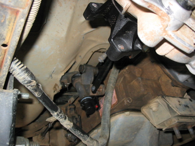 Undercarriage view with black bracket, wiring loom, and hoses on a tan frame