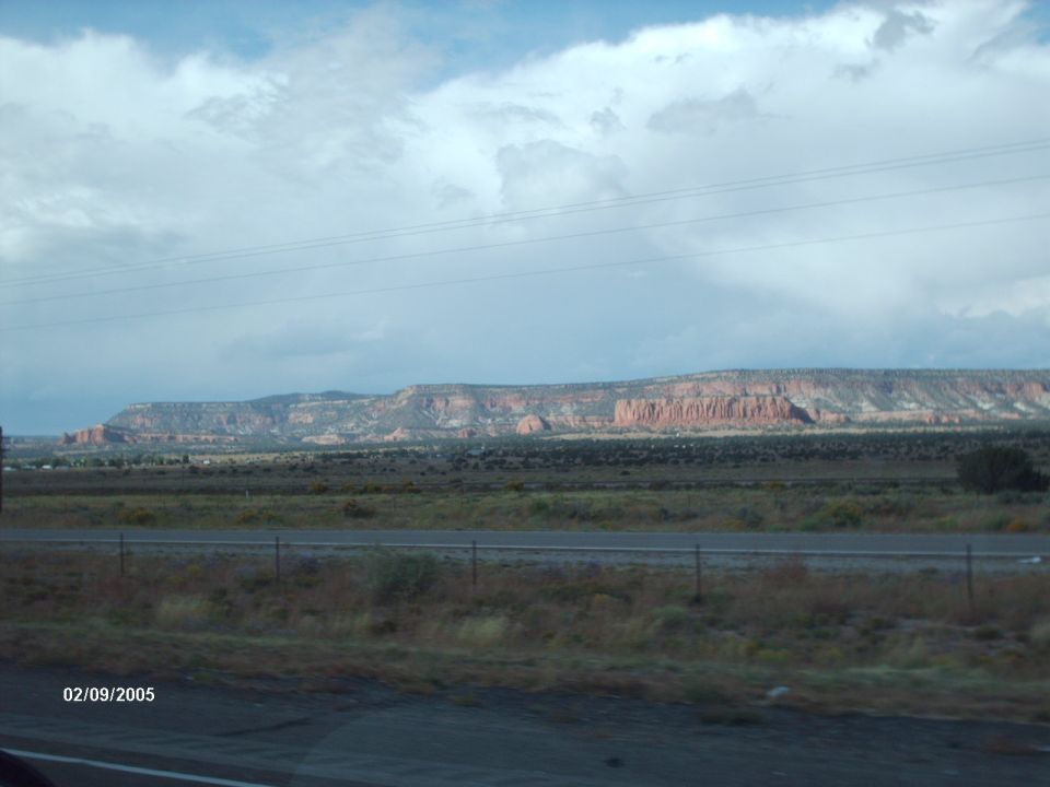 Desert landscape with mesas under a cloudy sky, highway in foreground