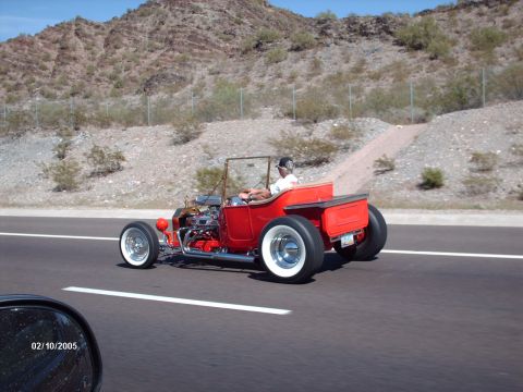 1995 Ford Probe - A classic red hot rod roadster with wide whitewall tires cruises down a desert highway.