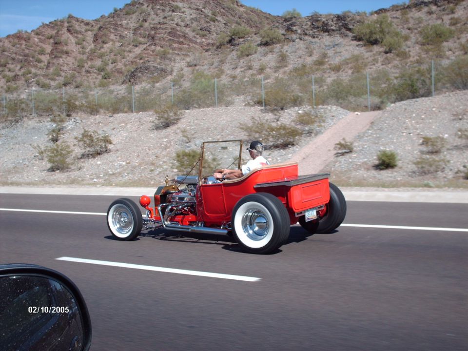 Red hot rod roadster with wide whitewall tires driving on highway